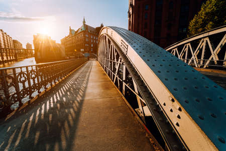 Metal arch bridge with rivets in the Speicherstadt of Hamburg during sunset golden hour with sunburst in horizonの写真素材