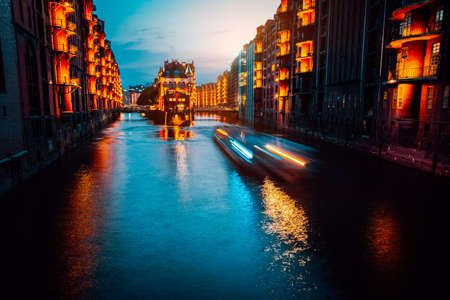 A colorfully illuminated boat cruising on the Wandrahmsfleet at night. The Warehouse District in Hamburg, Germany. The district is located within the HafenCity quarter. Long exposureの写真素材