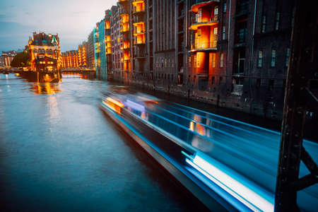 A colorfully illuminated boat cruising on the Wandrahmsfleet at night. The Warehouse District in Hamburg, Germany. The district located within the HafenCity quarter. Long exposureの写真素材