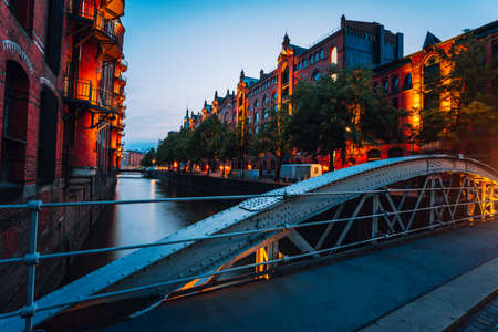 Touristic spot of old bridge and red brick illuminated buildings, canal and square in golden sunset light. Speicherstadt Hamburg. Warehause District at dawnの写真素材