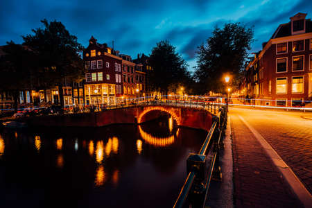 Amazing night in Amsterdam. Illuminated canal and bridge with typical dutch houses and bicycles, Holland, Netherlands. Lights trails from the bicycles. Long exposureの写真素材