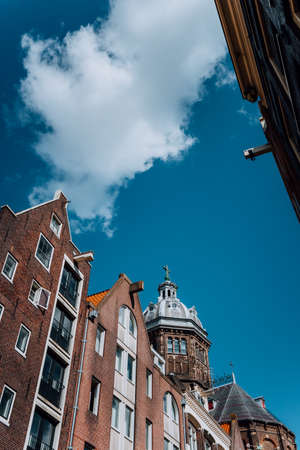 Low angle of narrow dutch houses with dome of St. Nicolas church in Amsterdam against blue sky and white cloudの写真素材