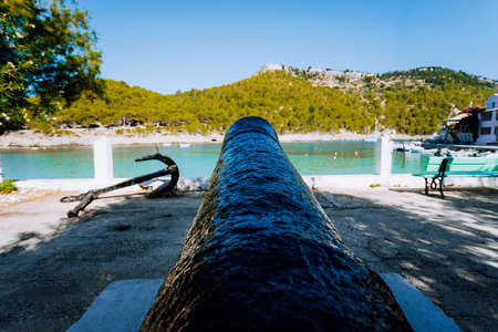Cannon and anchor on coast of Kefalonia island in Assos village. Tranquil sea bay and lush pine grove. Greeceの写真素材