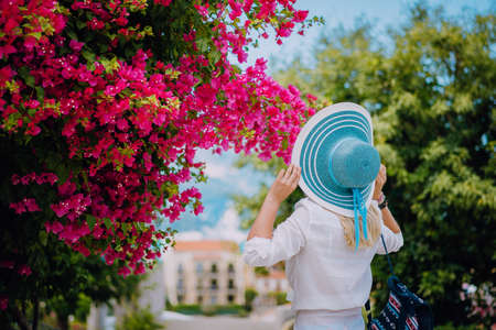 Elegant traveler woman with straw hat smelling beautiful colorful flowers on the islands of Greece during summer time. Romantic Traveling vacation conceptの写真素材