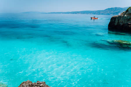 Small red boat floating on clear blue sea water. Summer beach vacation relaxation conceptの写真素材