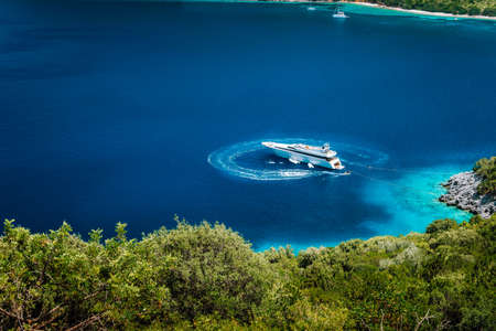 Luxury white yacht sail boat anchoring in a tranquil bay in deep blue water water, near picturesque shore of greek islandsの写真素材