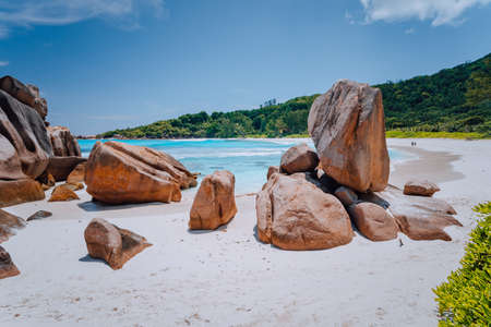 Couple on tropical beach lagoon with granite boulders in the turquoise water and a pristine white...