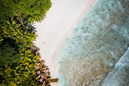 Girl sunbathing on tropical cocos beach with beautiful rocks, palm trees and ocean waves. Aerial drone shot. Seychellesの写真素材