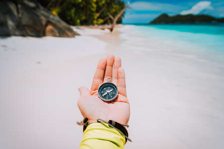 Hand with compass against tropical sandy beach and ocean. POV Travel conceptの写真素材