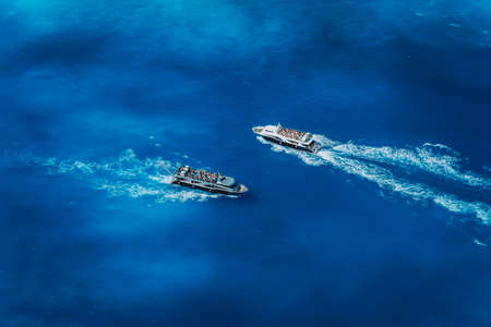 Two fully occupied tourist boats in open sea leaving and arriving in Navagio Beach on Zakynthos Island in Greeceの写真素材