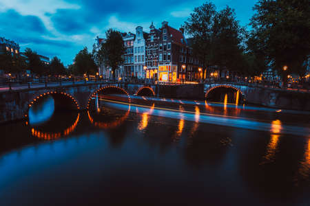 Bridge illumination and boat light trails in evening Amsterdam with reflection in Herengracht canal. Typical dutch houses in dusk light, Holland, Netherlandsの写真素材