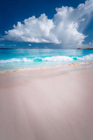 Beautiful white ocean wave rolling towards tropical sandy beach. Fluffy clouds above blue sea. Grand Anse, Seychellesの写真素材