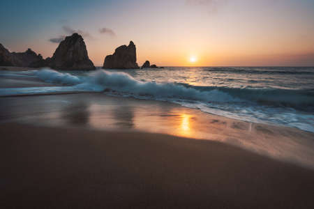Portugal Ursa Beach at atlantic coast. Sunset reflection. White wave roll towards sandy beach with...