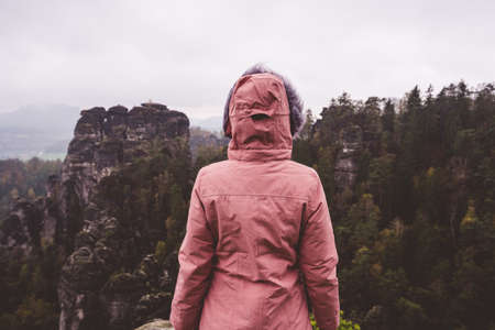 Young woman in outdoor clothing standing alone in front of jugged mountain top ridge with wild...