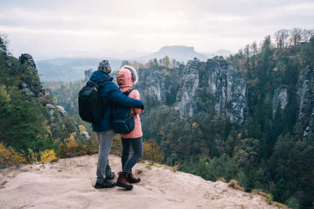 Young couple in outdoor clothing with backpacks standing on plateau enjoying view of mountain ridge and wild forest in the valley on hiking trail. Travel lifestyle conceptの写真素材