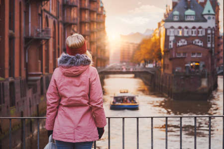 Adult woman tourist enjoying golden sunset light over the Elbe river with pleasure tour boat. Speicherstadt historical warehouse district of Hamburg, Germany, Europeの写真素材