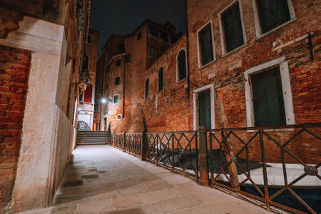 Gothic narrow streets with old red brick wall houses at night. Empty alleyways and bridge stairs in Venice, Italyの写真素材