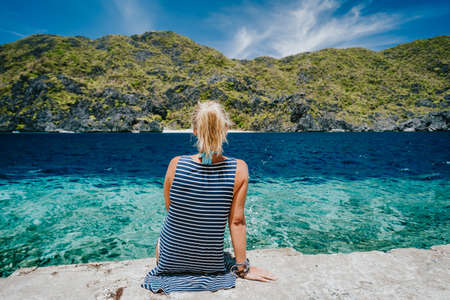 Tourist female rear view sitting on Matinloc dock pier enjoying tapiutan strait on island hoping...