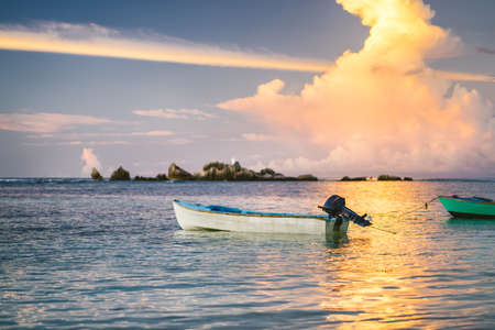 Purple golden clouds lit by sunset on La Digue. An fishing boat floats in ocean bay with fire colors on horizonの写真素材