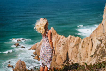 Beautiful blond women enjoying ocean breeze on coastline of Praia da Ursa Beach in morning light. Surreal scenery of Sintra, Portugal. Atlantic Ocean coastline landscapeの写真素材