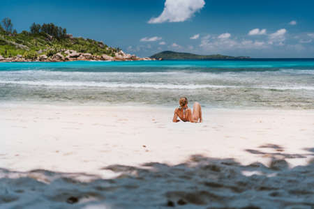 Young tanned woman enjoying tropical sandy beach Anse Cocos at La Digue Island, Seychelles