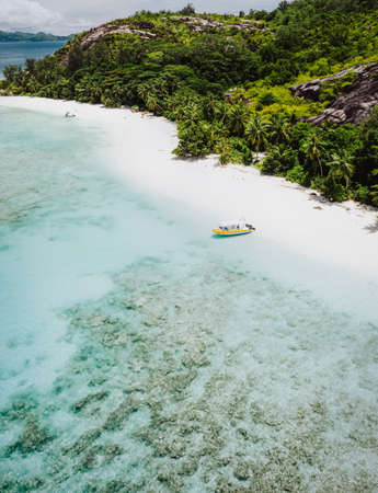 A aerial view of untouched sandy beach with palm trees and lonely tourist boat in blues clear lagoon on Therese Island of Mahe, Seychellesの写真素材