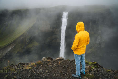 A man in yellow jacket enjoying Haifoss waterfall on rainy overcast weather. Highlands of Icelandの写真素材