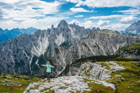Aerial view of a woman hiker in green jacket with raised hands admiring Cadini di Misurina mountain...