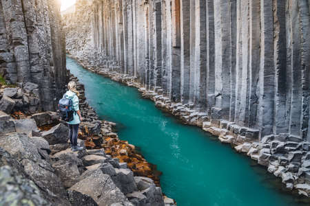Woman hiker with backpack enjoying Studlagil Canyon. Unique Jokulsa basalt colums and A Bru river....
