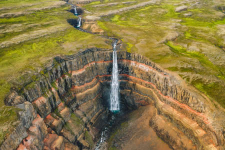 Aerial view of the Hengifoss waterfall in East Iceland. Hengifoss is the third highest waterfall in Iceland and is surrounded by basaltic strata with red layers of clay between the basaltic layersの写真素材