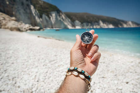 Hand holding a compass on the beach in backgroundの写真素材