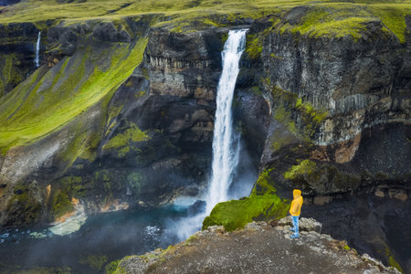 Man in yellow coat admire Haifoss Waterfall in Landmannalaugar canyon, Iceland. Aerial panoramic drone viewの写真素材
