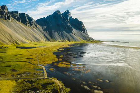 Aerial view of stunning scene of Stokksnes cape with Vestrahorn. Panoramic Icelandic view of black sand dunes by tide with yellow grassの写真素材