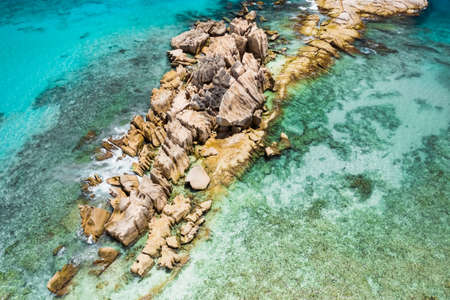 Aerial top view of ocean waves hitting granite rocks on the beach in La Digue, Seychelles