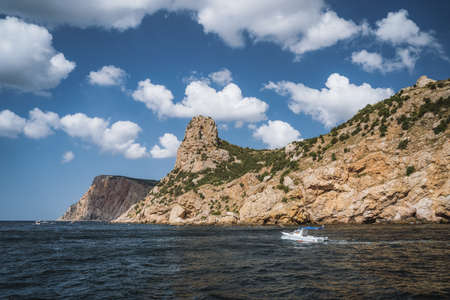 Tourist day trip pleasure boat moves along beautiful cliff landscape with white clouds in sky. Balaklava. Black sea Crimeaの写真素材