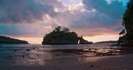 Island silhouette at sunset in shallow calm ocean water with dark cloudy colorful sky on Crystal Bay Beach in Bali Indonesia.の写真素材