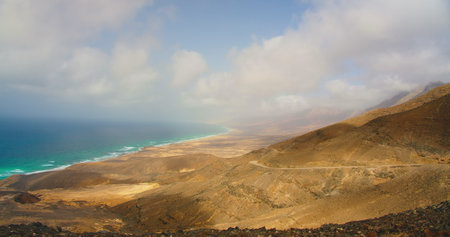 Cofete beach with endless horizon and traces on the sand. Cloudy weather. Volcanic hills in the background and Atlantic Ocean. Playa de Cofete is longest on Fuerteventura, Canary Islands, Spain.の写真素材