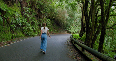 Woman walks along an asphalt road in a dense forest. Overgrown trees in laurel tree forest or jungle, Anaga National Park, Tenerife, Canary Islands, Spain.の写真素材