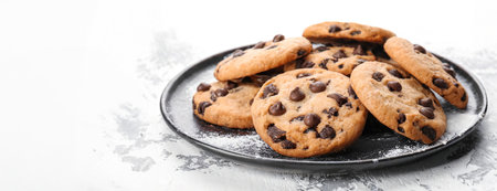 National Cookie Day yummy chocolate crispy cookies served on a plate on white table background. Powdered sugar on the kitchen surfaceの素材