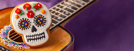 Close-up of a skull shaped cookie decorated with colorful icing, placed on an acoustic guitar, symbolizing Dia de los Muertos celebrations..の素材