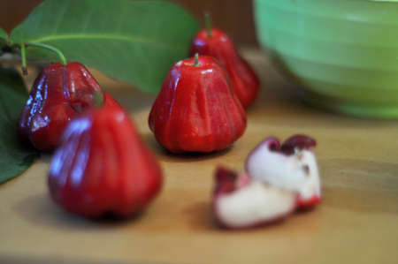 red guava fruit with green leaves on a wooden table