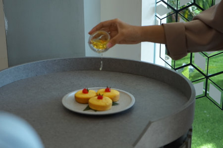 Woman pouring honey from a glass into a plate of cake on the tableの写真素材