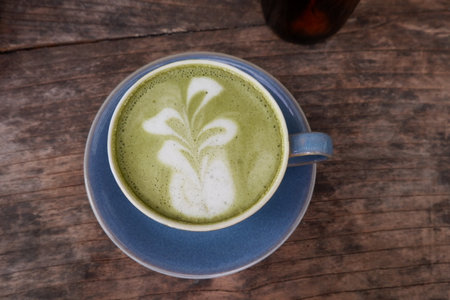 A cup of green tea with latte art on wooden background.