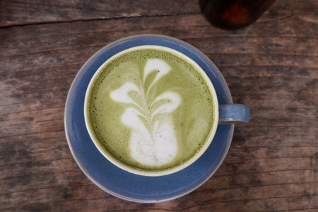 Green tea latte art in blue cup on wooden table background.