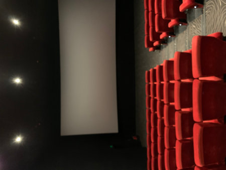 Cinema auditorium with red seats and white screen in the darkの写真素材