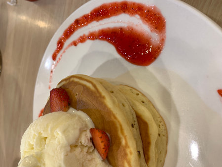 Pancakes with ice cream and strawberry jam on a white plate