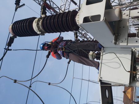 Electrician working on high voltage power lines in electrical substation.