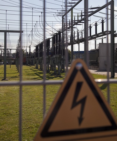 electric cables with ceramic parts near a plant with green grass and electrocution danger signの写真素材