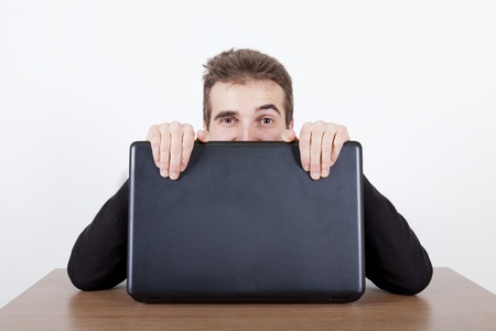 young man hiding behind a laptop on a desk