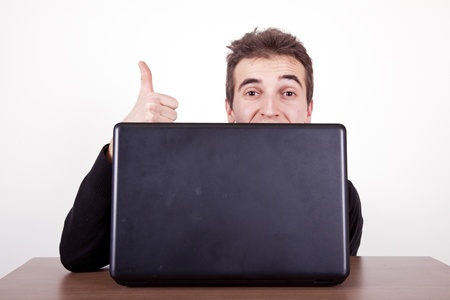 young man holding thumbs up with a laptop on a deskの写真素材